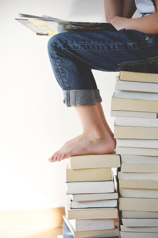 girl in jeans sitting on stack of books